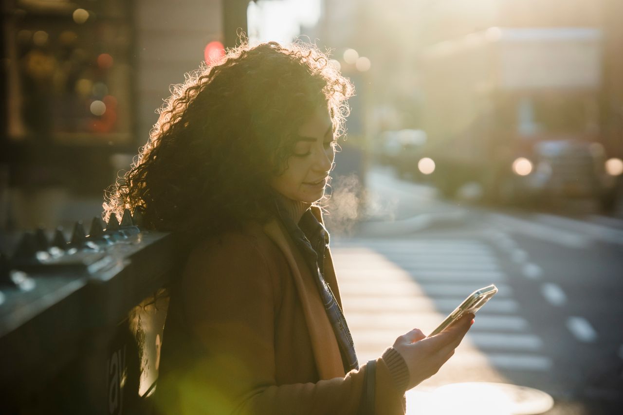 A customer checking her smartphone on a sunlit city street