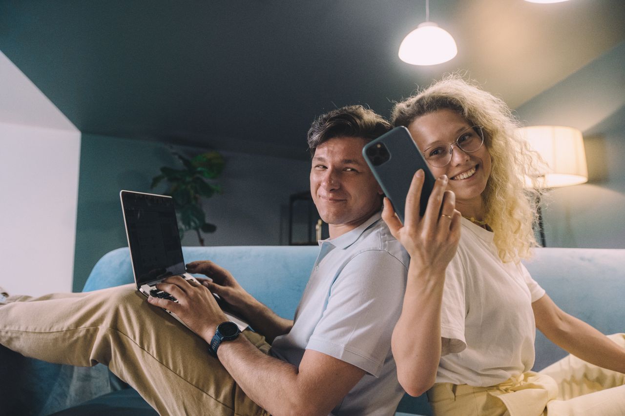 A couple using a smartphone and laptop together at home
