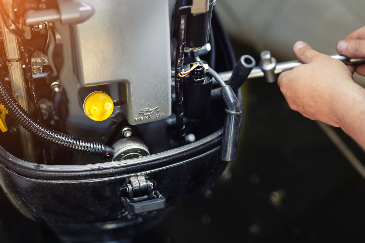 A marine mechanic working on an outboard engine with its cover removed