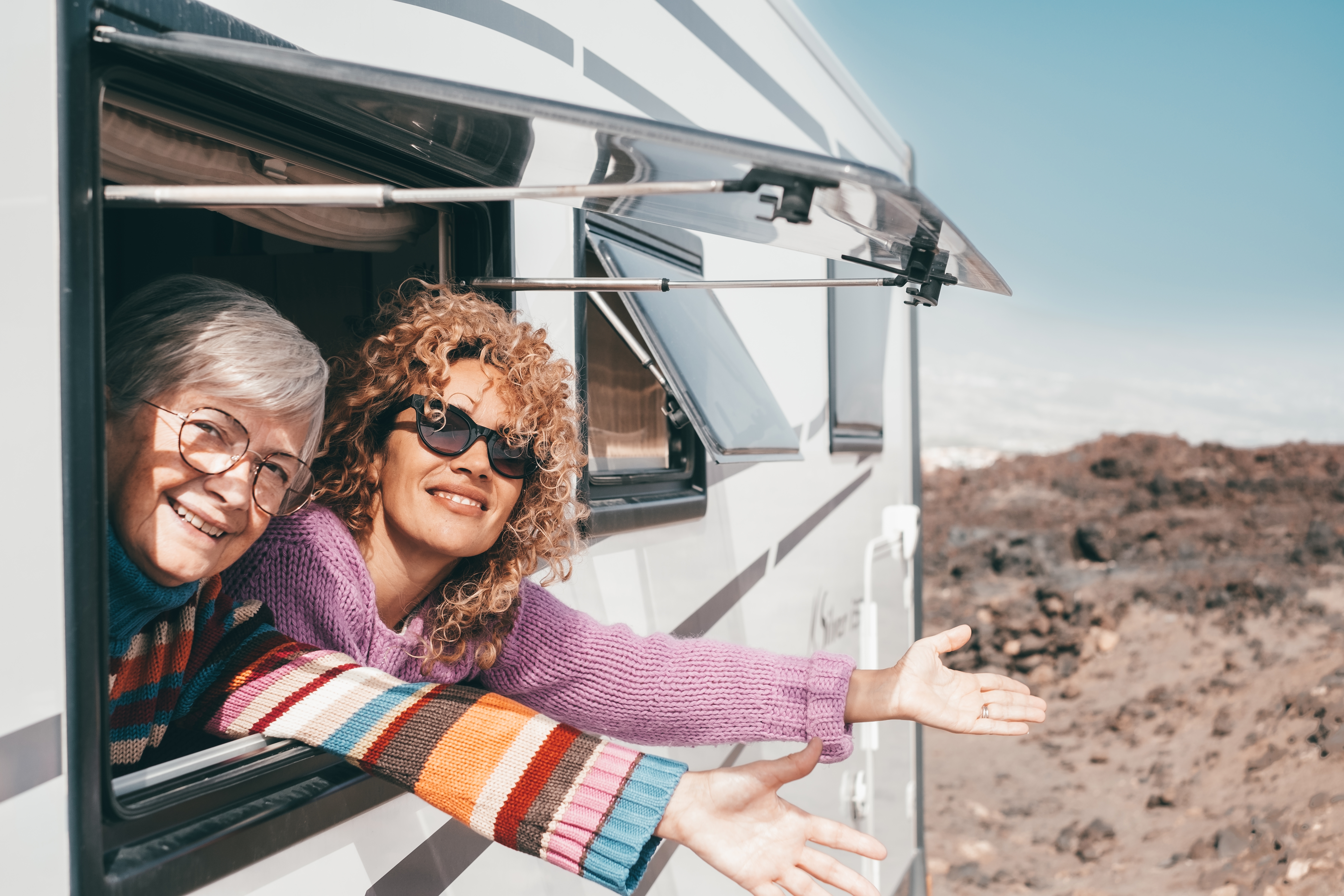 Two smiling women enjoying a road trip from the window of their motorhome