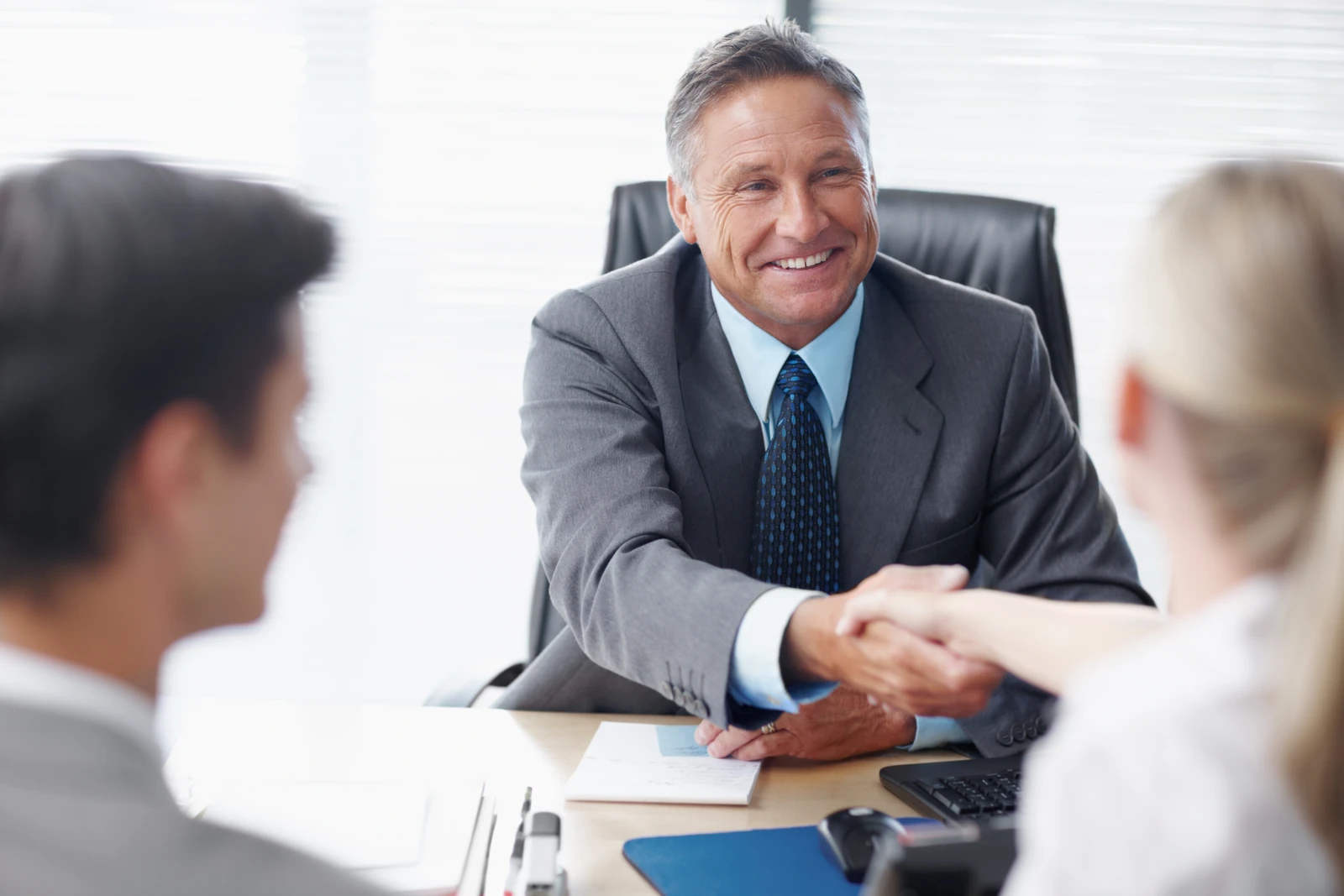 A business consultant smiling and shaking hands with a client at his desk
