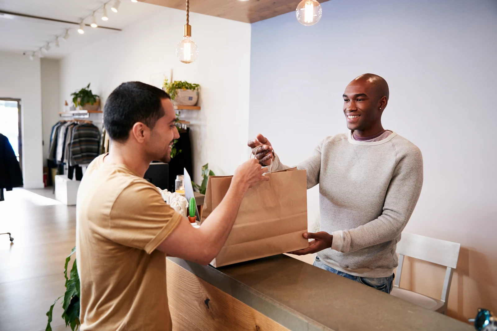 A smiling store employee handing a shopping bag to a customer at the counter