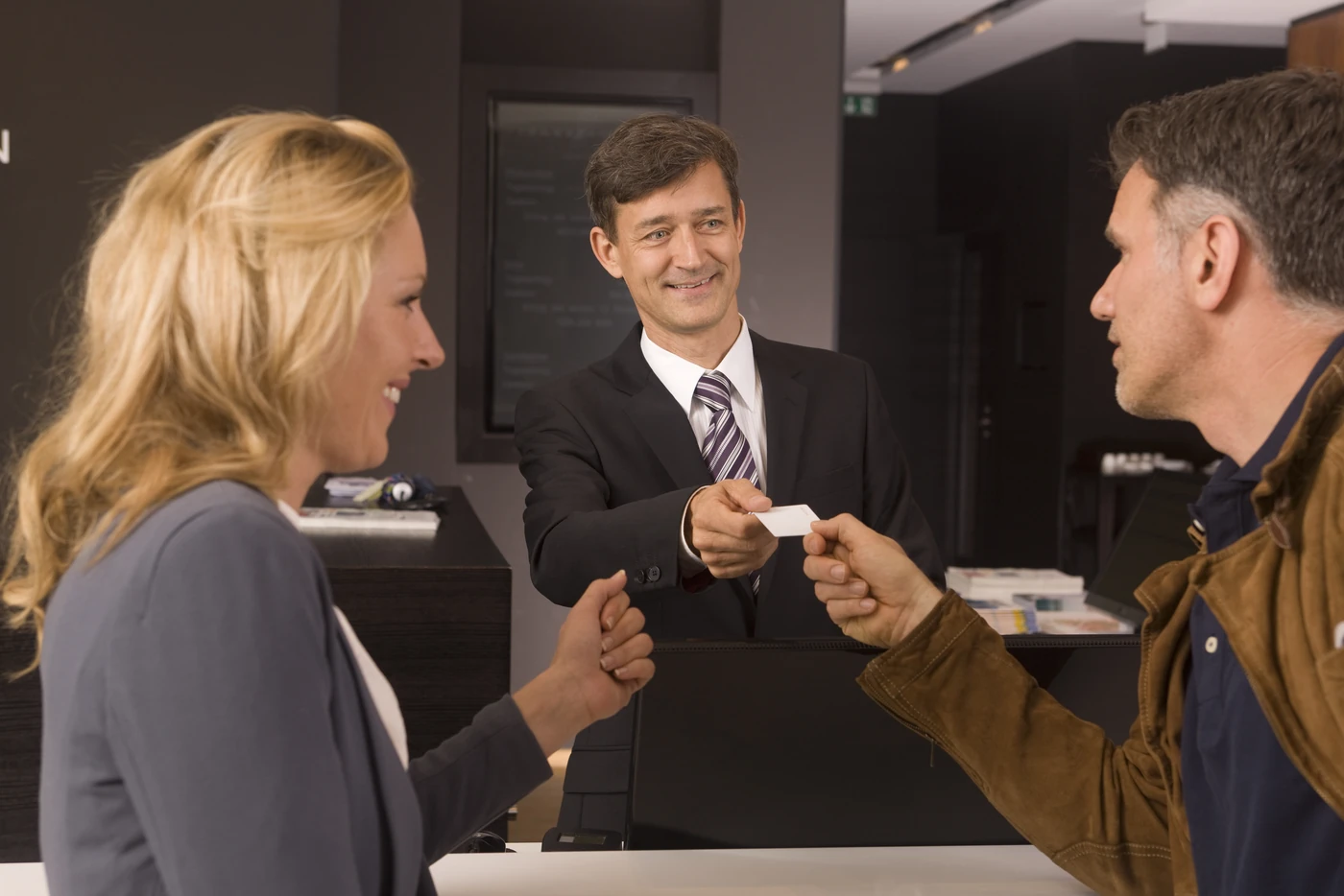 A hotel receptionist smiling as he welcomes a couple and hands them their room key