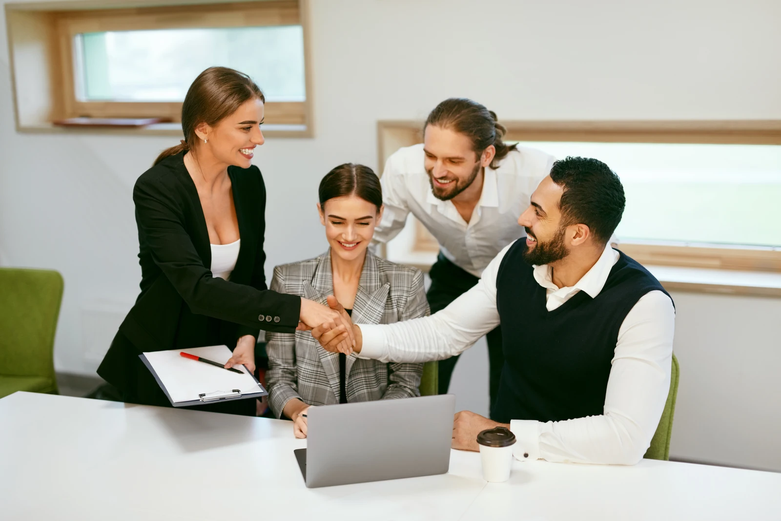 Business professionals smiling and greeting each other with a handshake at an office table