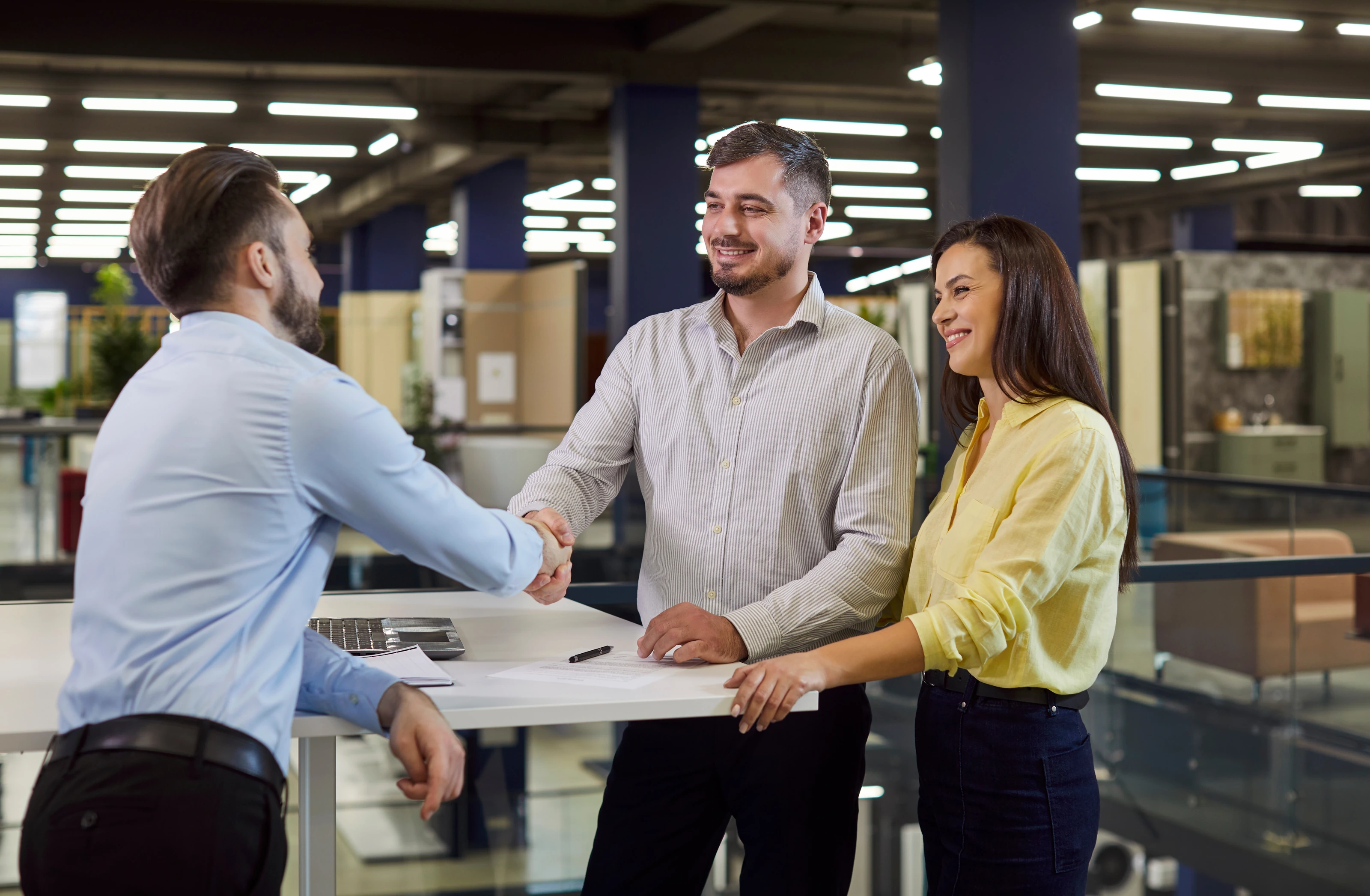 A shop consultant greeting a smiling couple in a furniture showroom.