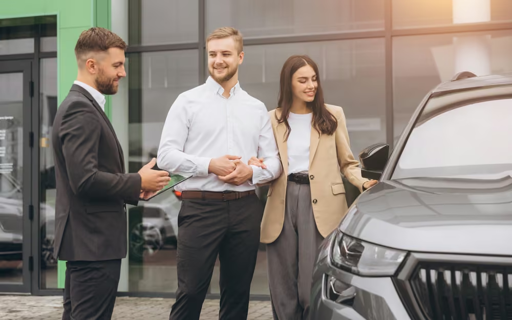 A couple speaking with a sales advisor outside a vehicle showroom.