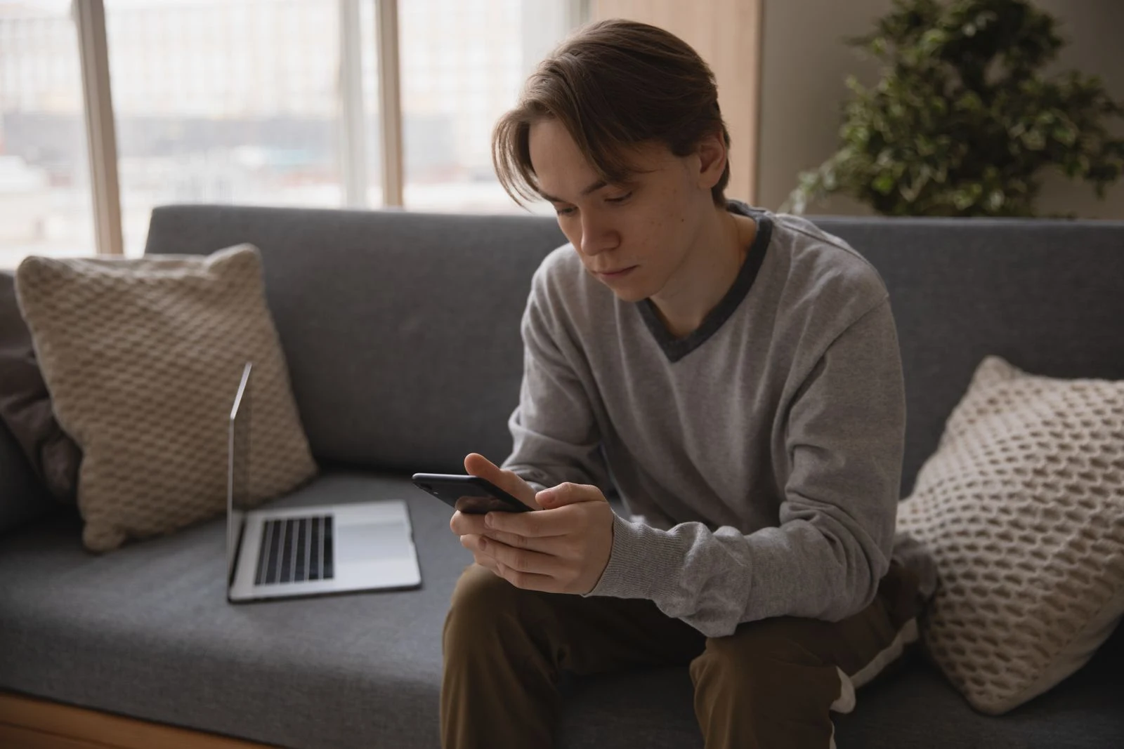 A person at home using a smartphone beside an open laptop