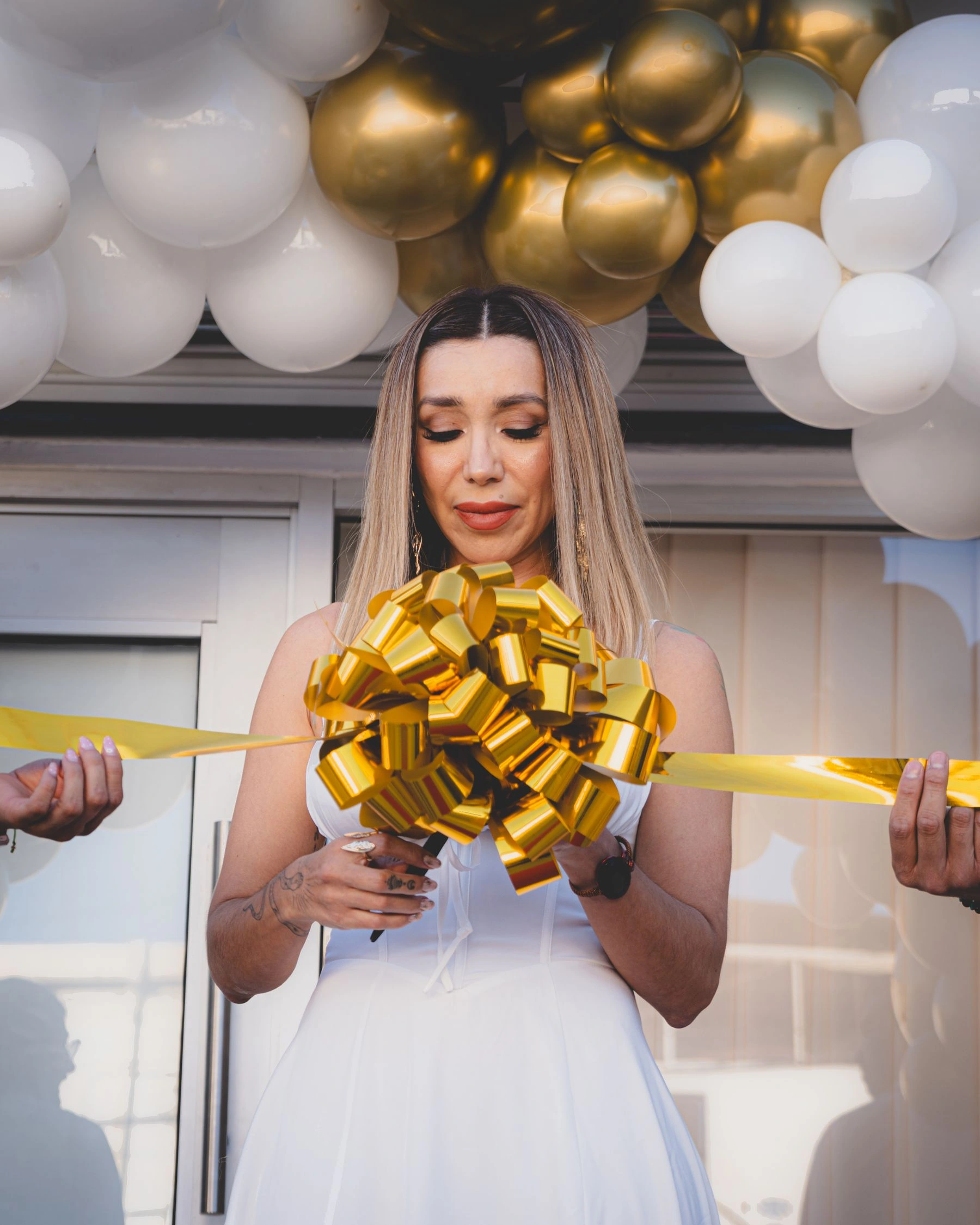 A business owner cutting a gold opening ribbon beneath gold and white balloons