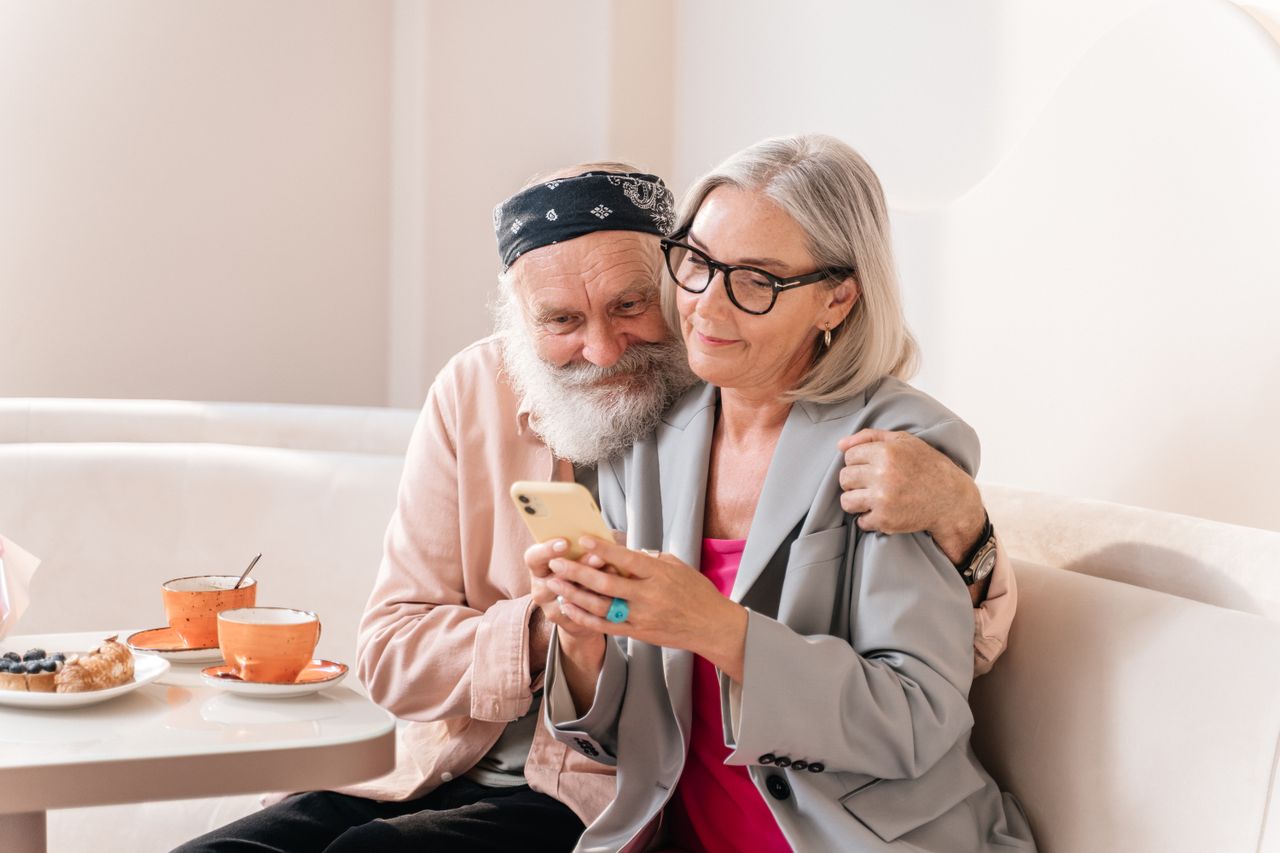 A couple smiling together as they browse a phone at a cafe