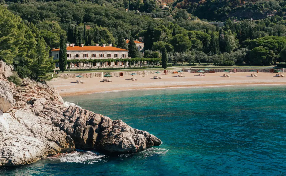 This image shows the Villa Miločer resort located on the coast of Montenegro, nestled along a picturesque pink sandy beach.