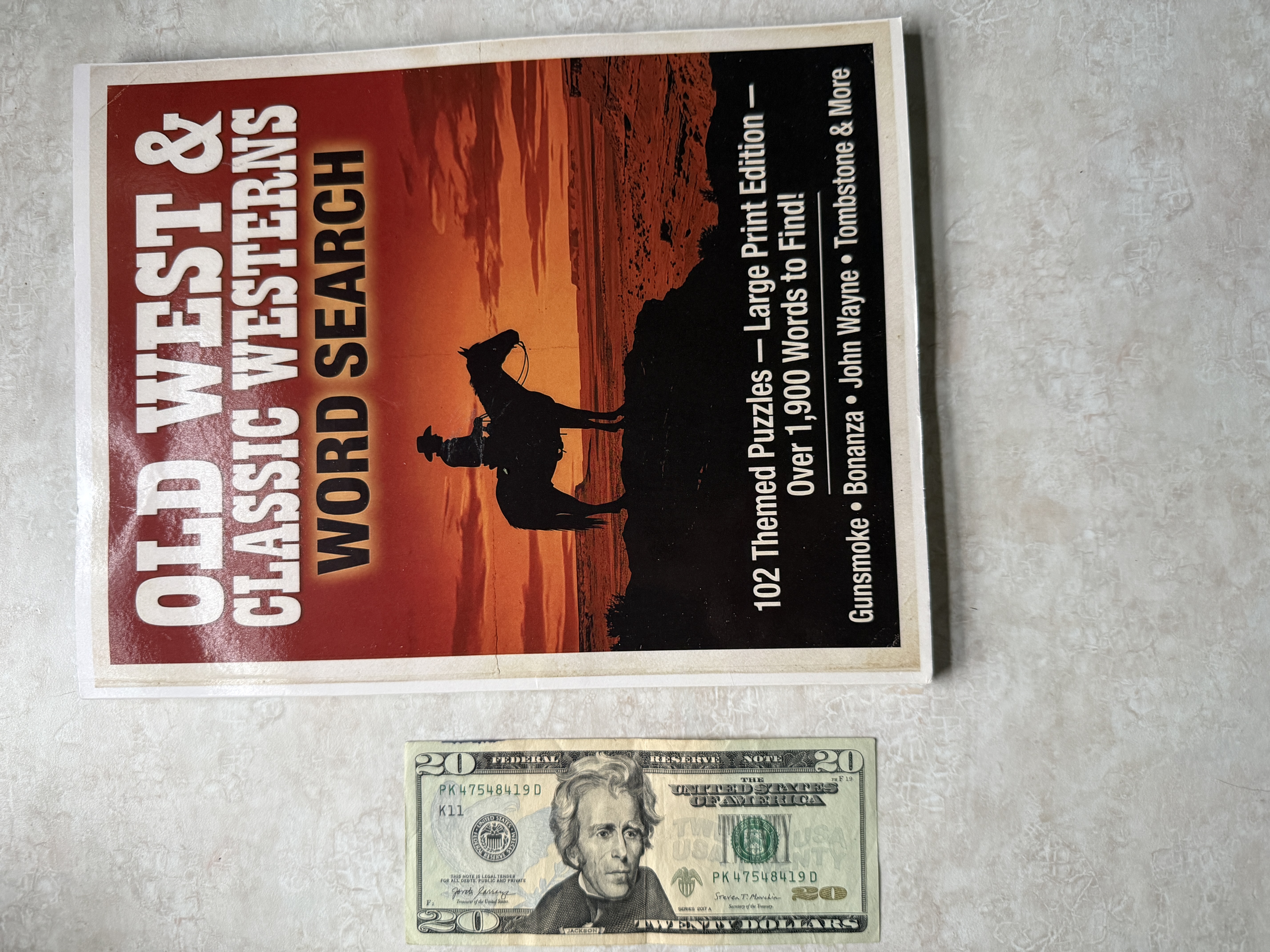 Our word search book next to a $20 bill — grid letters bigger than the bill text