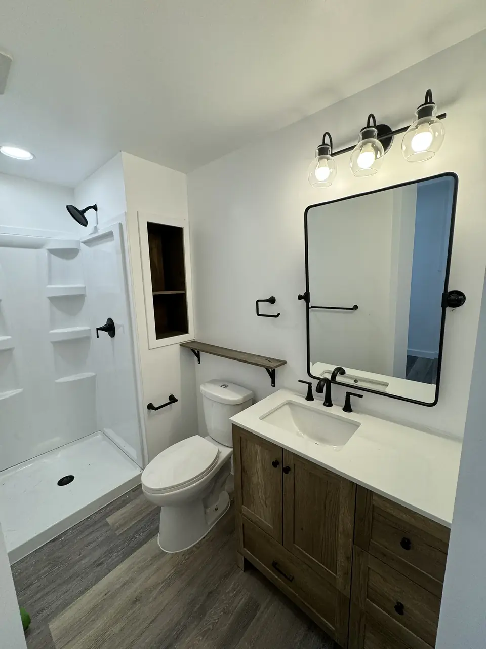 Remodeled bathroom with a wood vanity, black fixtures and a white shower