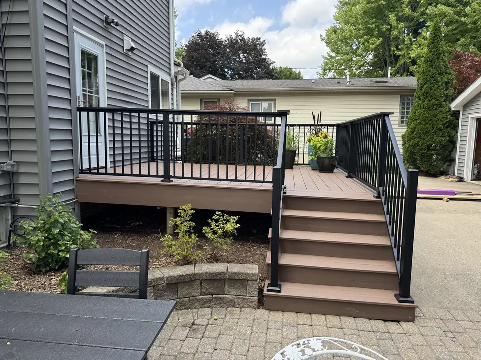 Brown deck with black railings and broad stairs opening onto a paved patio