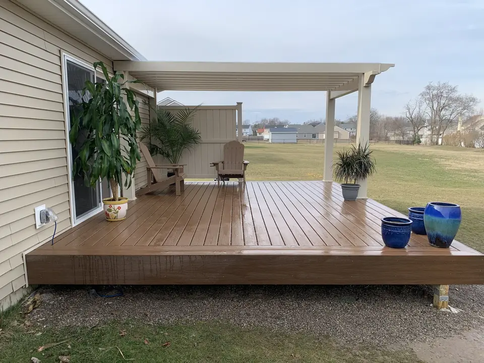 Brown deck with a white pergola, privacy screen and potted plants