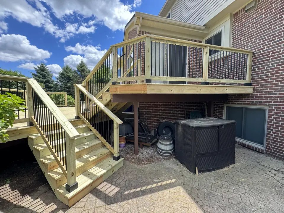 Raised wood deck with black balusters and stairs to a paved patio
