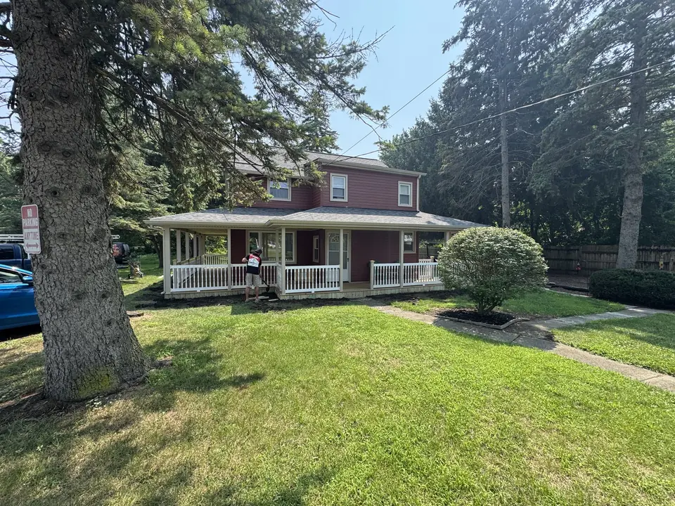 Red two-story home with a covered wraparound porch and white railings