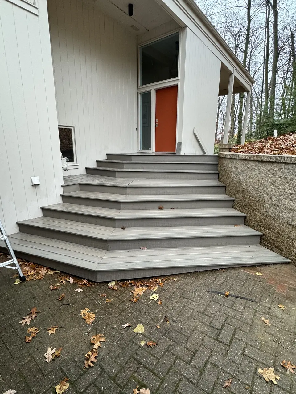 Broad gray composite entry steps beside a white home with an orange door