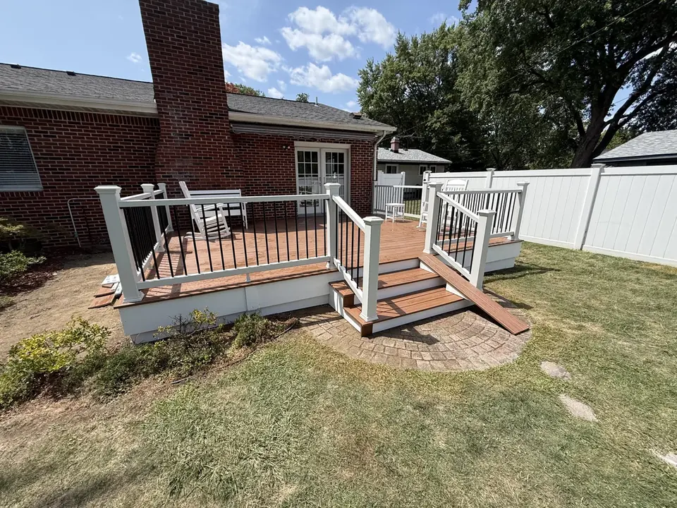 Deck with white railings and contrasting stair treads beside a brick home