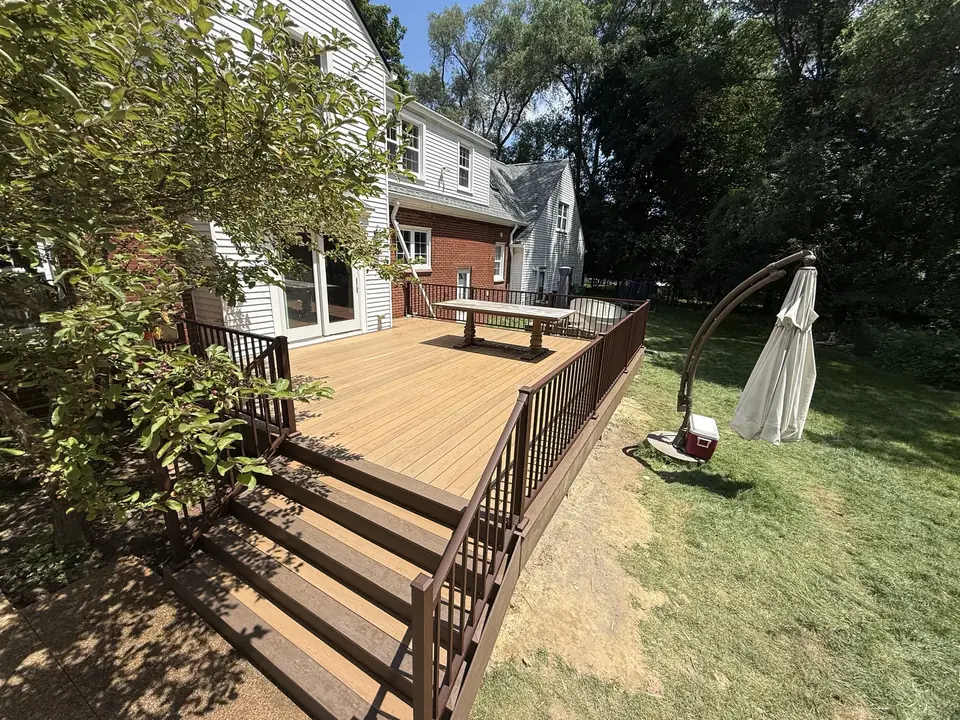 Wood deck with brown railings and wide steps beside a white and brick home