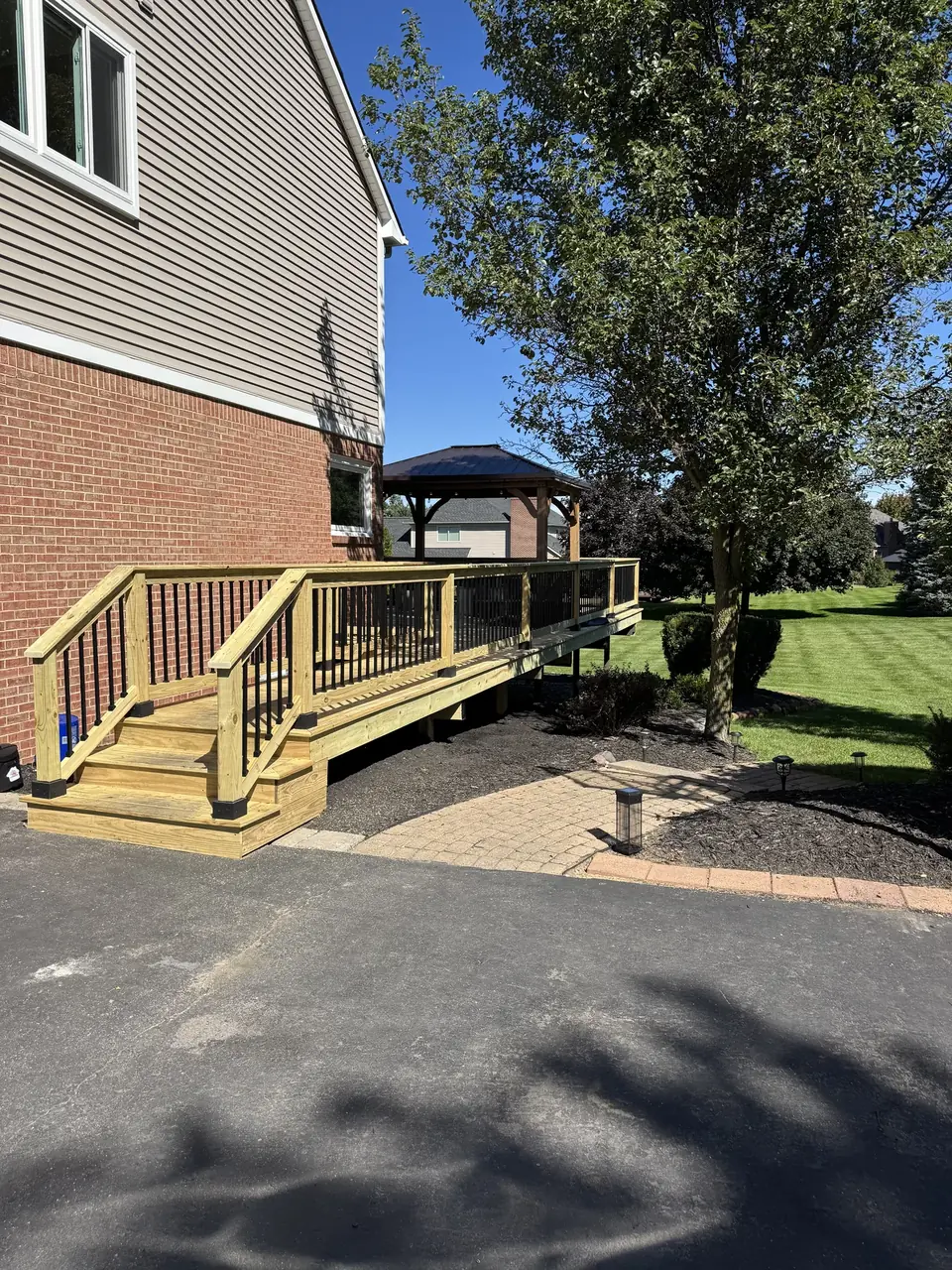 Long wood ramp with black balusters beside a brick and white-sided home