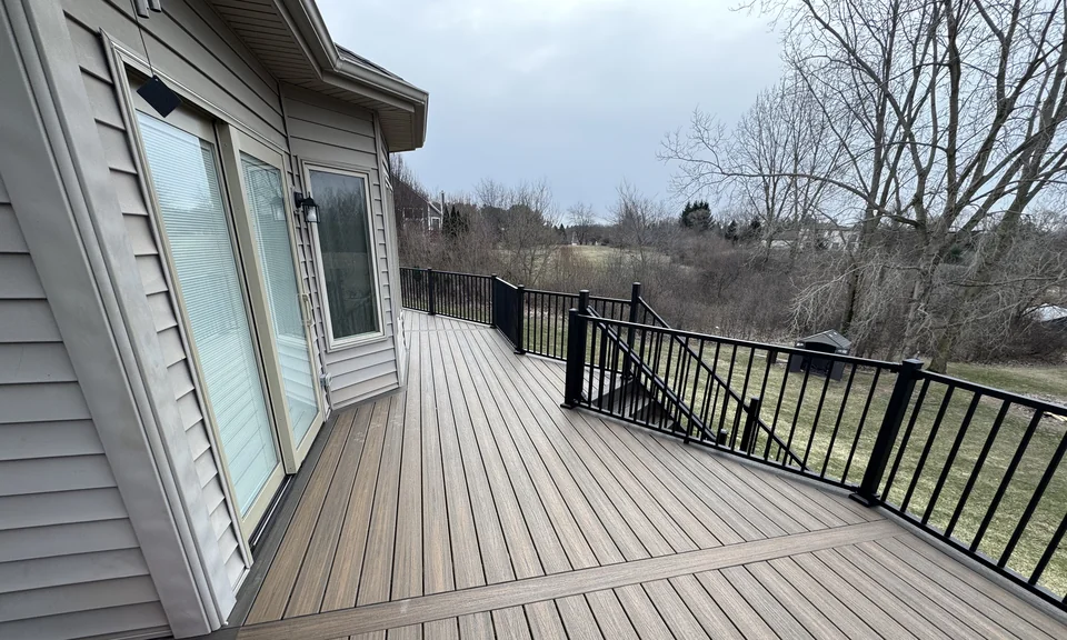 Gray deck beside a house with dark railings and a stair opening.
