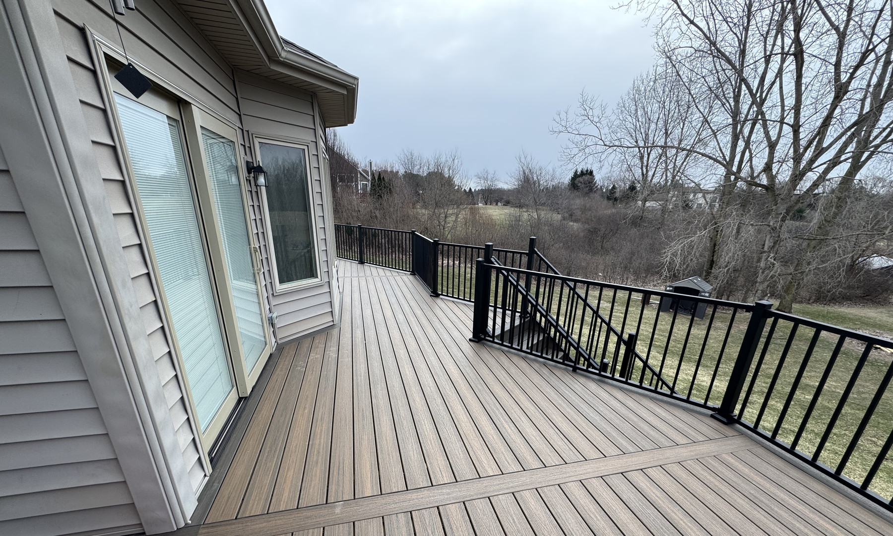 Gray deck beside the house, with dark railings, a projecting window wall and an opening for the steps.