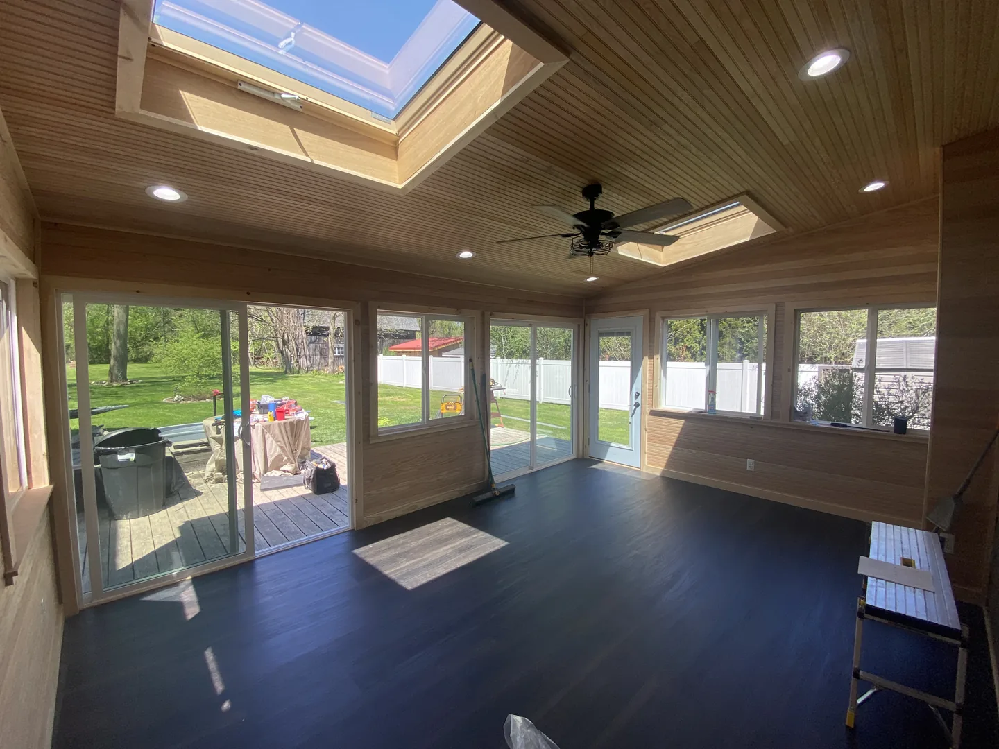 Room with wood-lined walls and ceiling, a skylight, windows, glass doors and a dark floor.