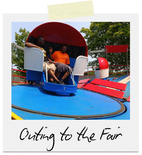 Outing to the Fair: Two men sit in a red, white, and blue fair ride.