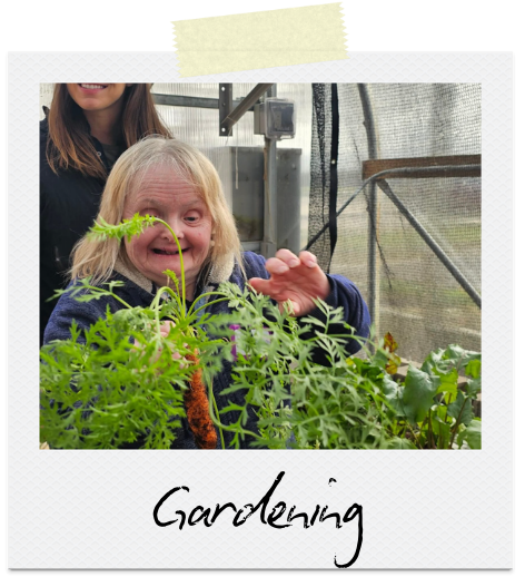 Gardening: A blonde woman in a blue jacket stands behind a leafy green plant.