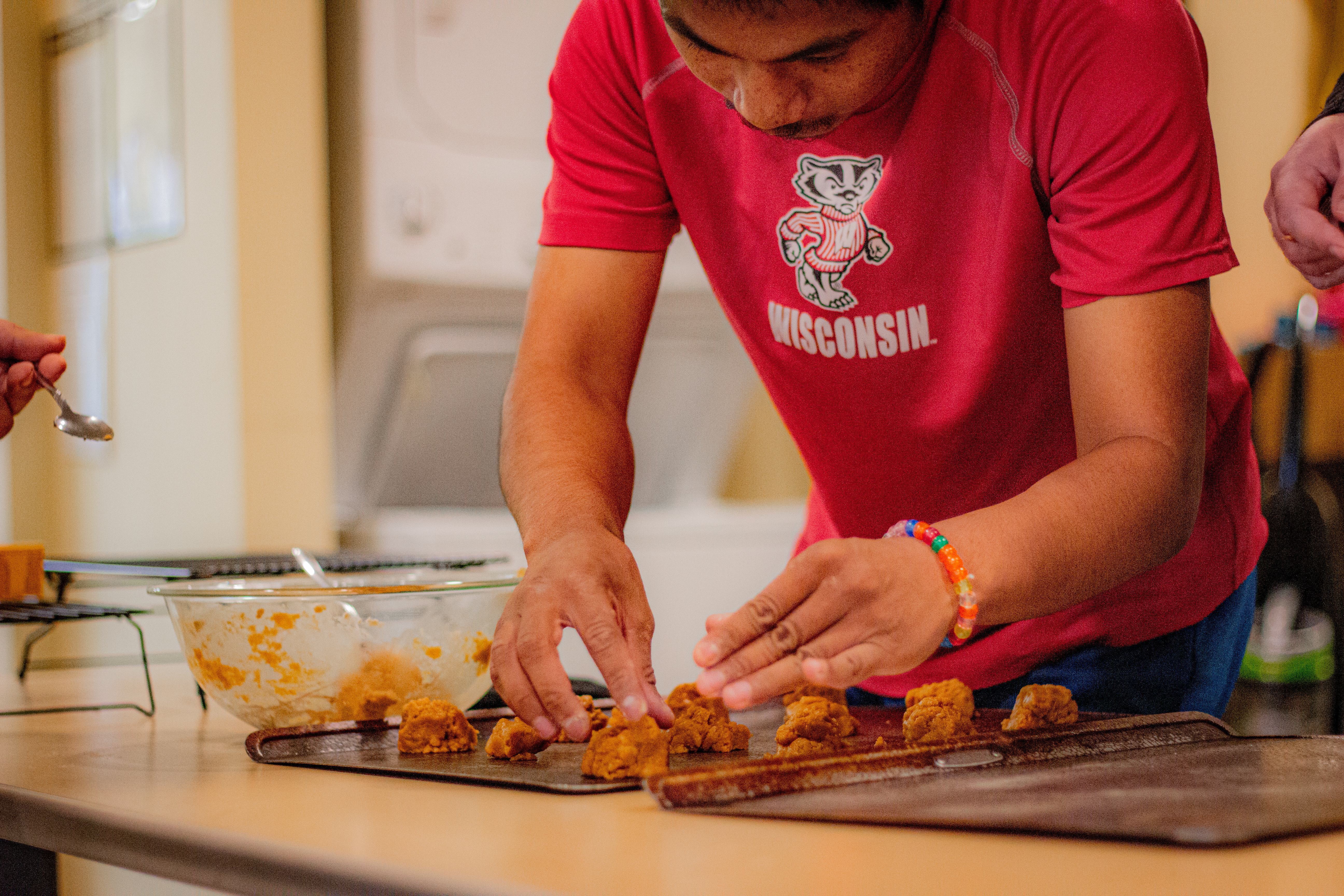A man in a red shirt arranging cookie dough on a baking sheet.