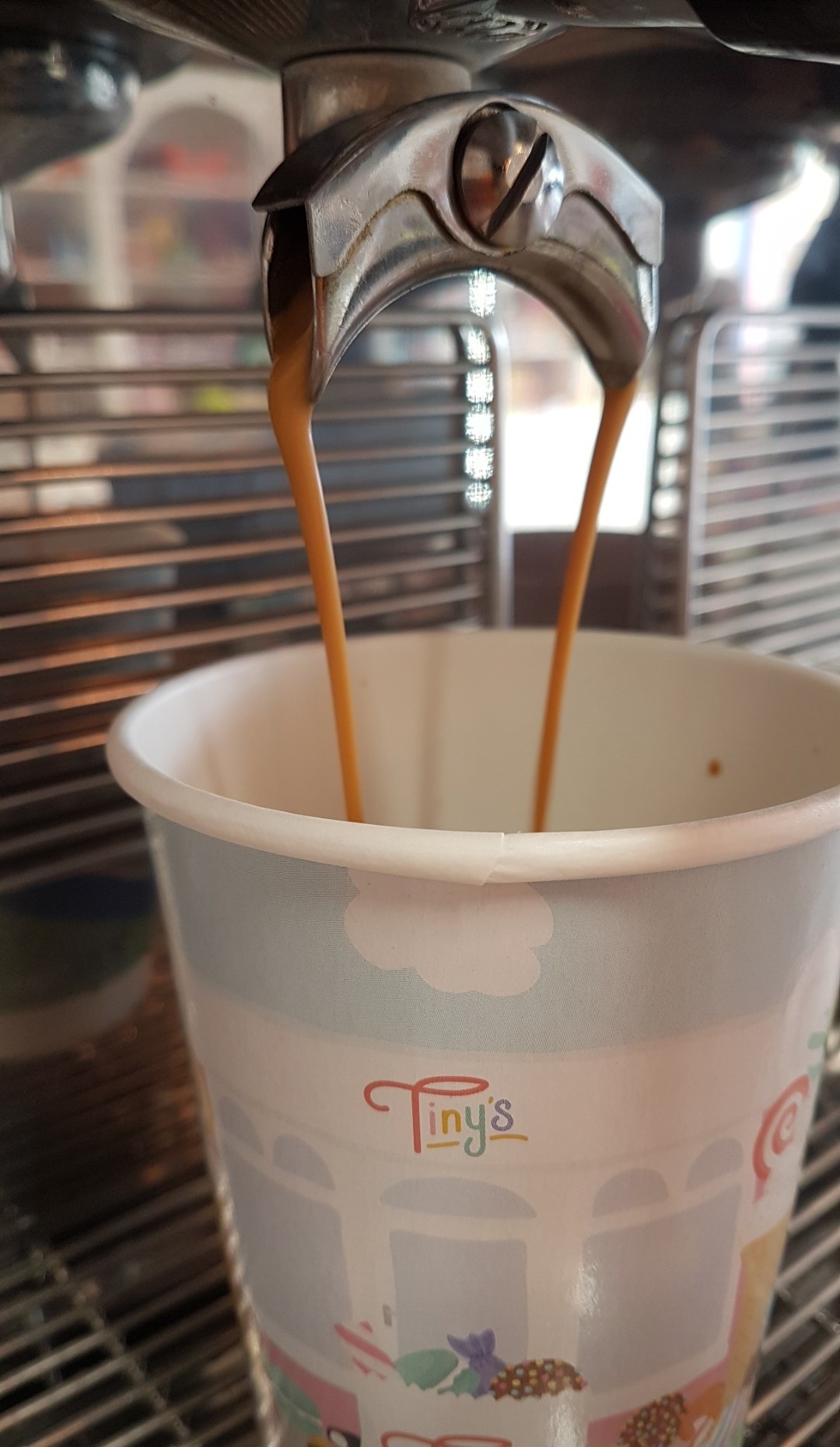 Espresso pouring from the coffee machine into a branded Tiny's cup