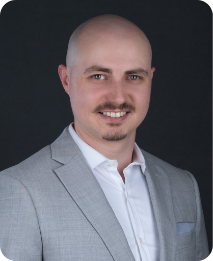 Professional headshot of Gabriel Rapacz, Vice-President and Co-Owner, wearing a light gray blazer and white shirt against a dark gray background.