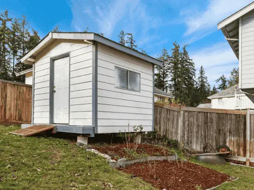 Small backyard garden shed sitting in the grass surrounded by trees.