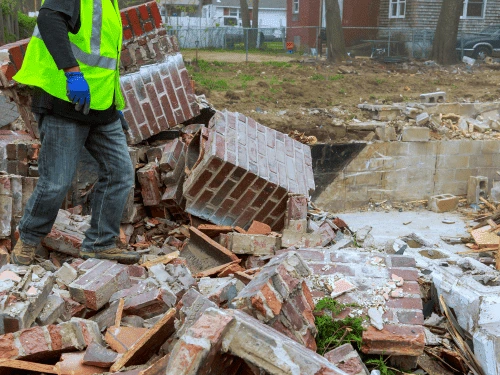 A crew member in a high-visibility safety vest surveying a recently demolished brick structure during a Newnan site cleanup.