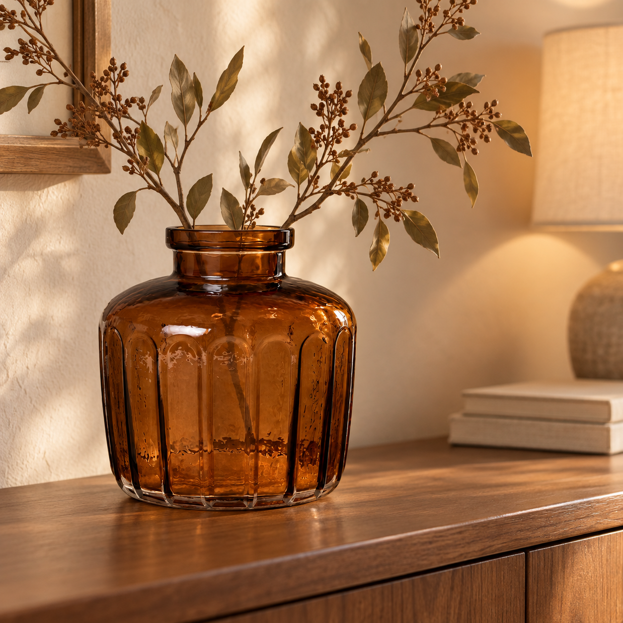 An amber ribbed glass vase with dried branches on a console