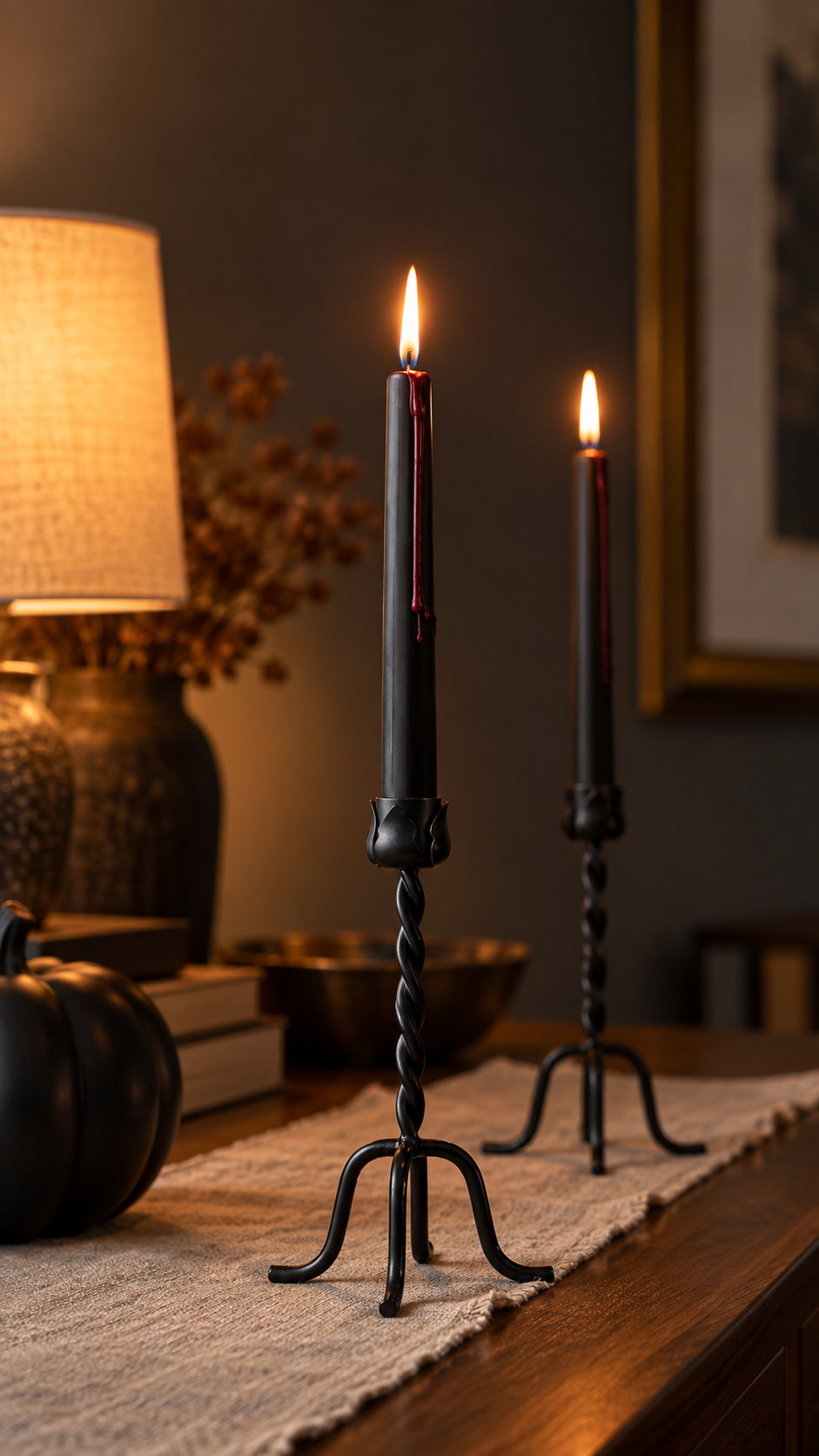 Black metal taper holders with black bleeding taper candles lit on a wood surface