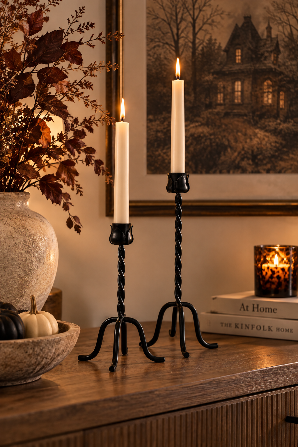 Two black twisted metal taper candle holders with lit ivory taper candles on a wood console