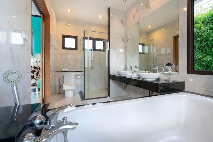 Un intérieur élégant comprenant un canapé crème, un fauteuil gris de style mid-century, une table basse en bois et quatre suspensions dorées devant un mur texturé avec des panneaux cannelés.