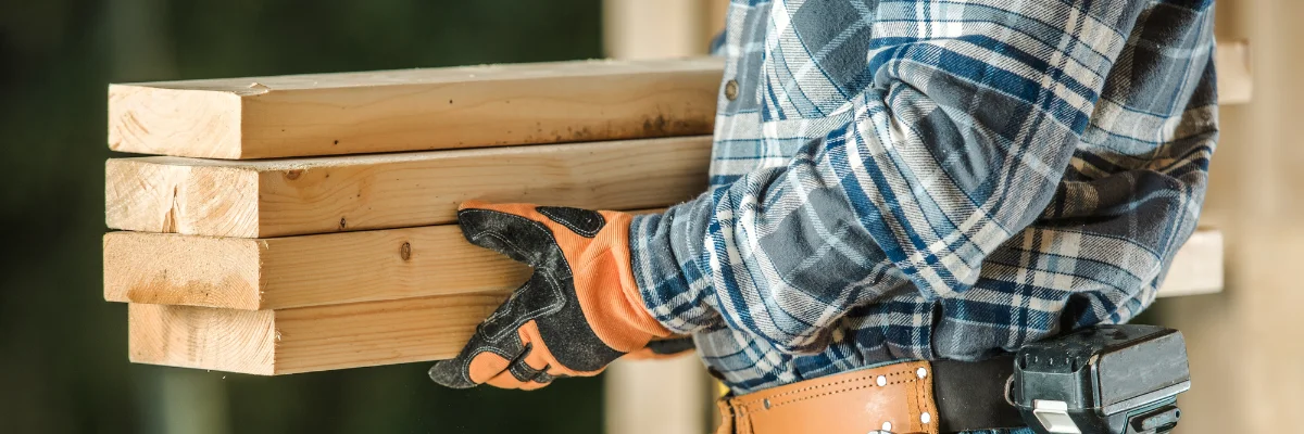 Construction worker carrying stacked lumber boards on job site.