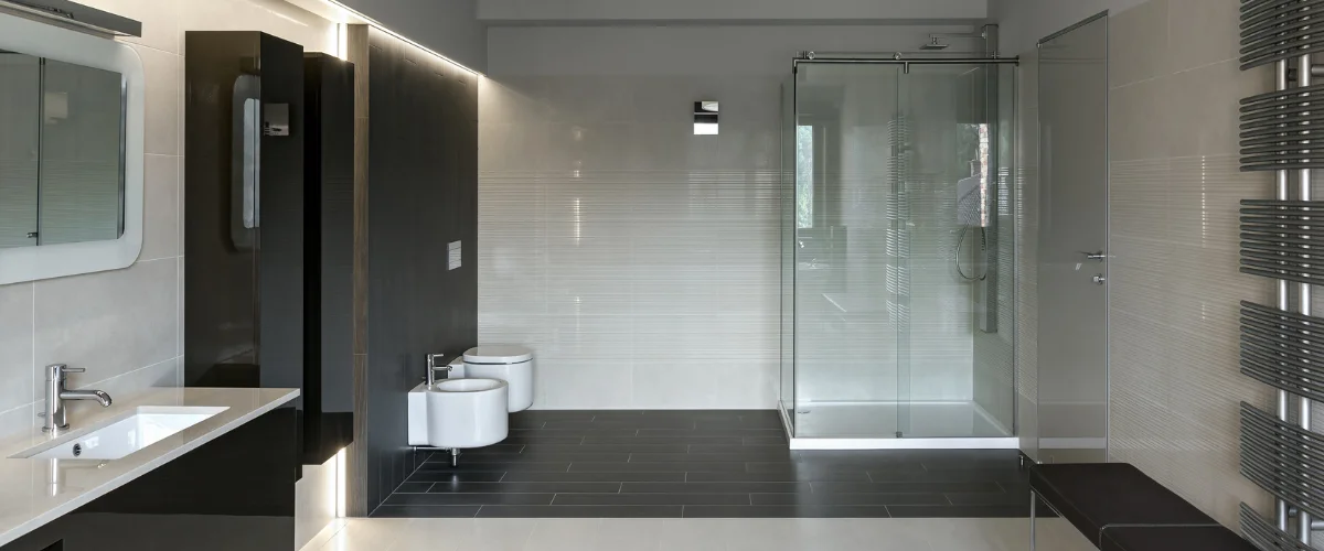 A modern bathroom with a freestanding white bathtub, a double vanity with square sinks, and dark tiled walls.