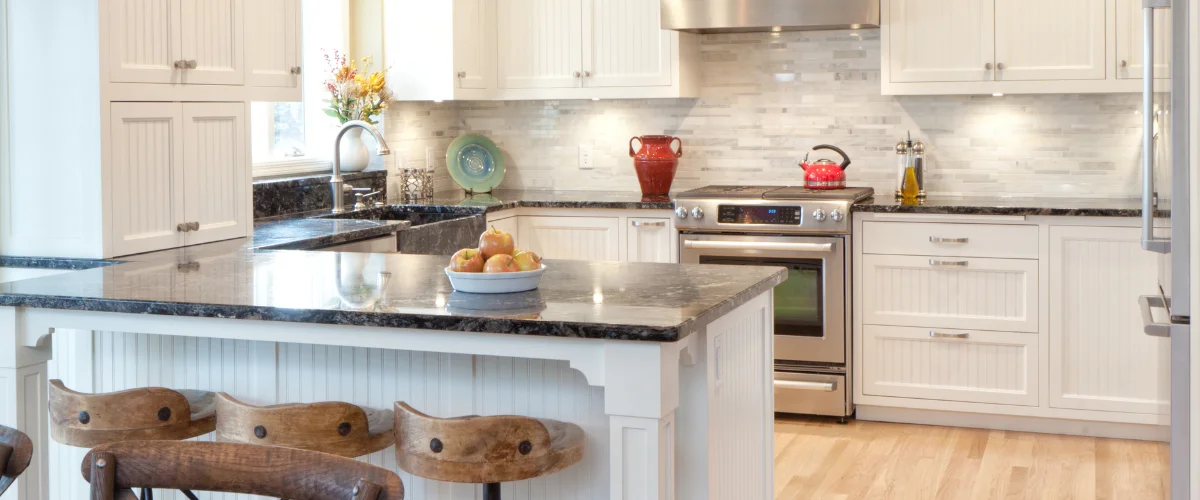 A classic white kitchen featuring white shaker cabinets, dark granite countertops, and a kitchen island with bar stools.