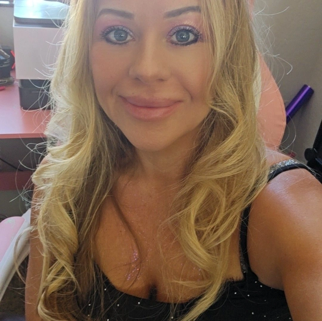 Owner of Landscape Medics smiling, with long blonde hair and pink makeup, looking at the camera indoors.