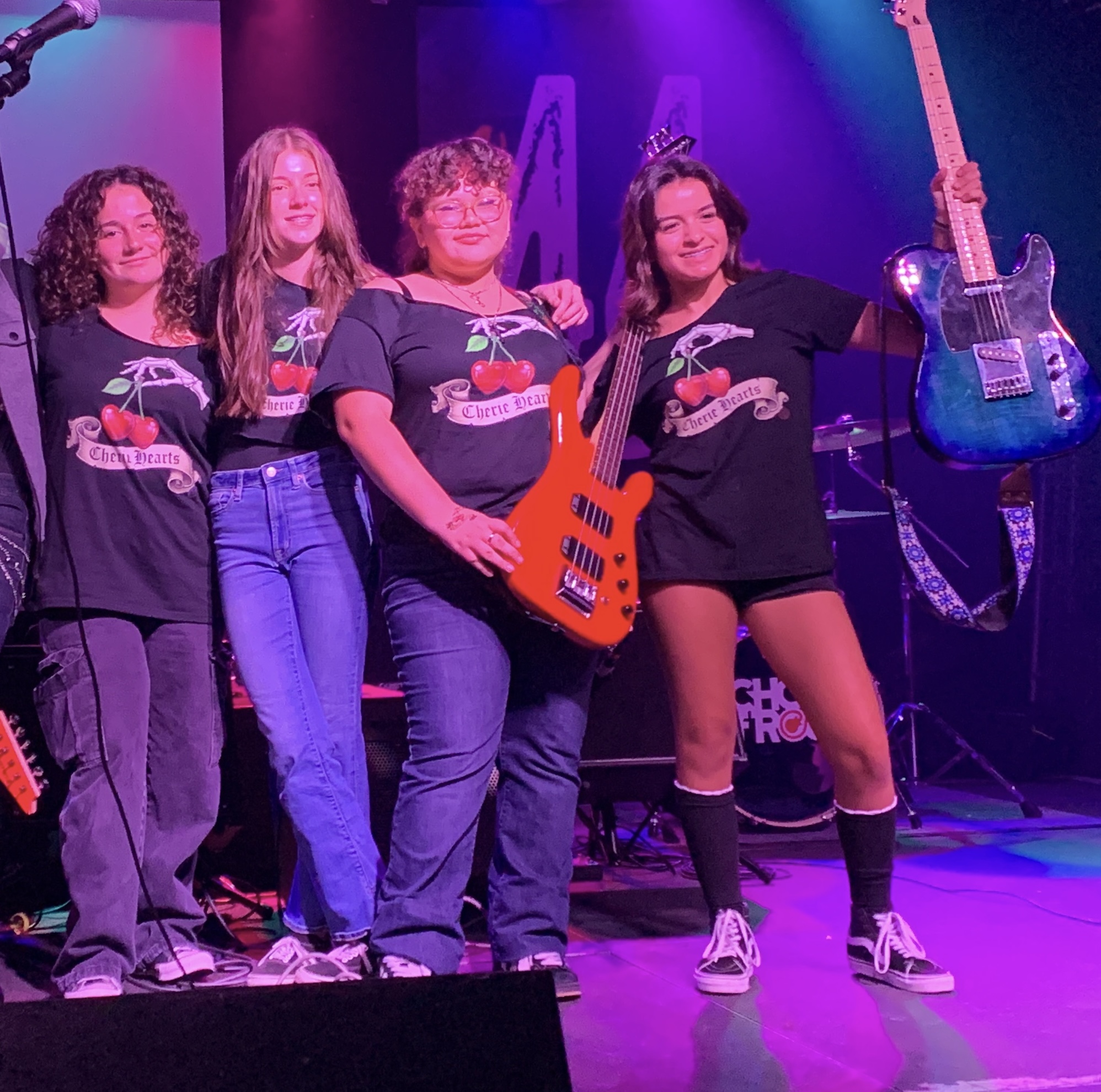 Cherie Hearts on stage in matching band shirts, guitars raised