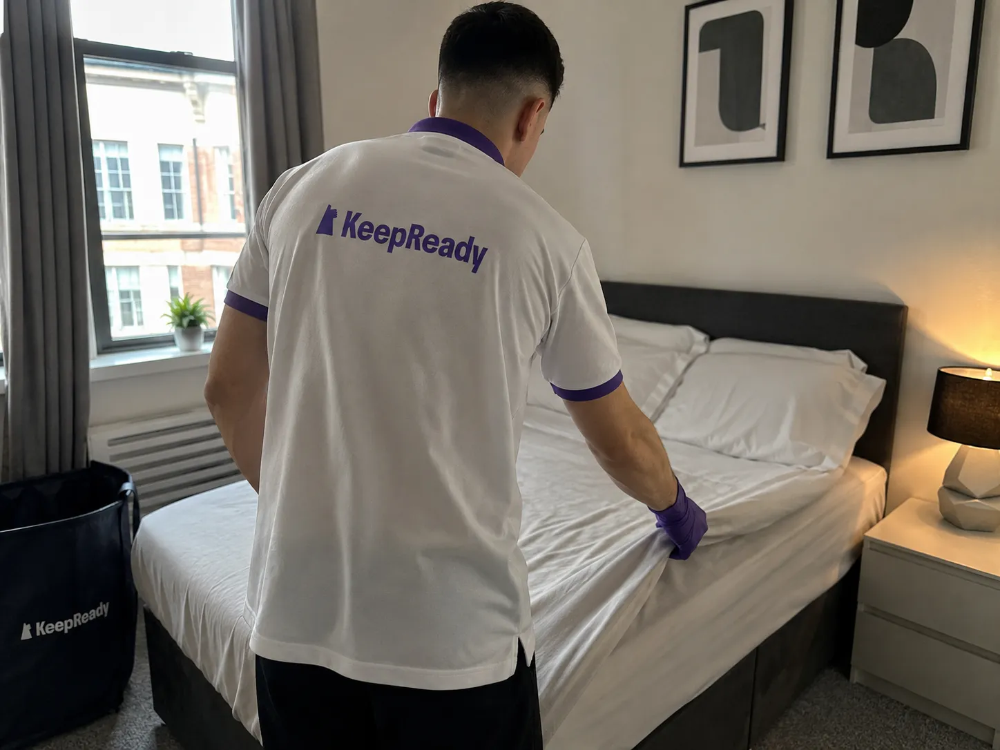 KeepReady professional in branded uniform making a bed with fresh linen during a property turnover service