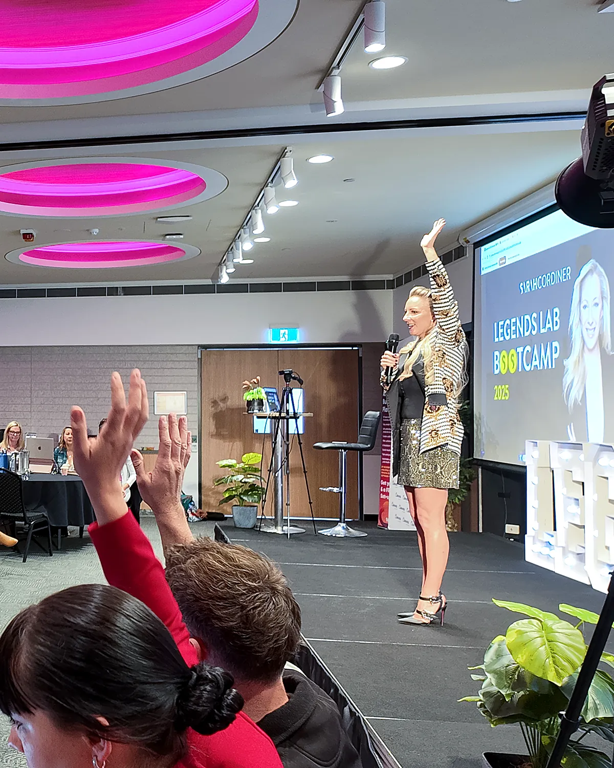 Sarah Cordiner on stage presenting the Legends Lab Bootcamp with the audience raising their hands
