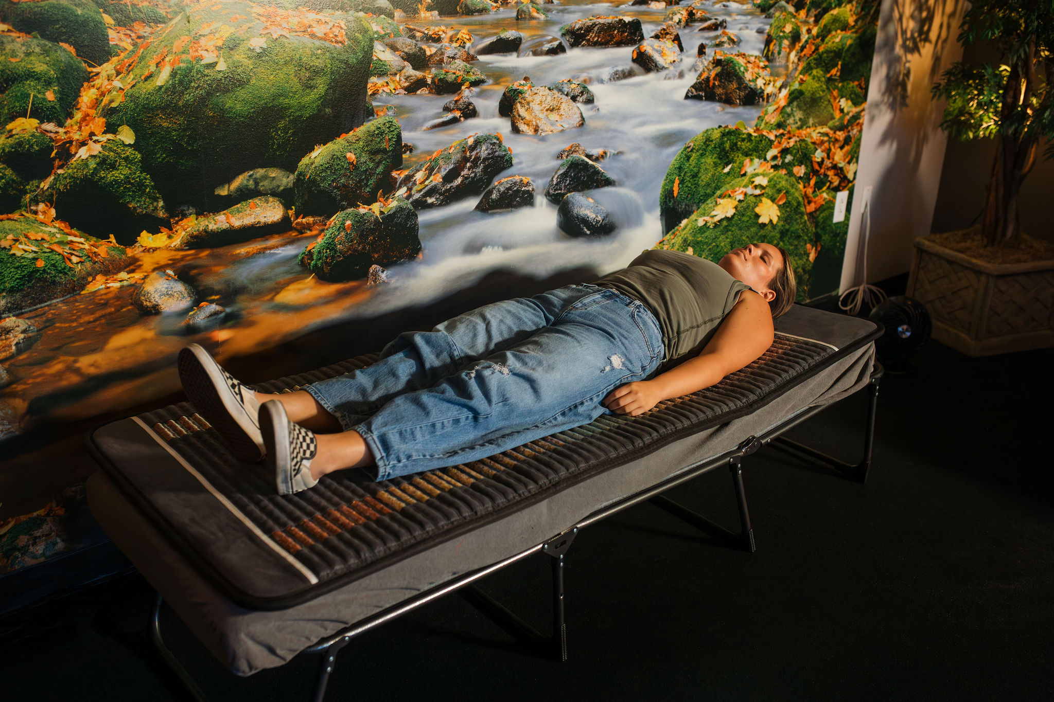 A woman in a green tank top and blue jeans laying on the AO Infinity Mat in front of a mural of a river in the Energy Lounge at SEWC.