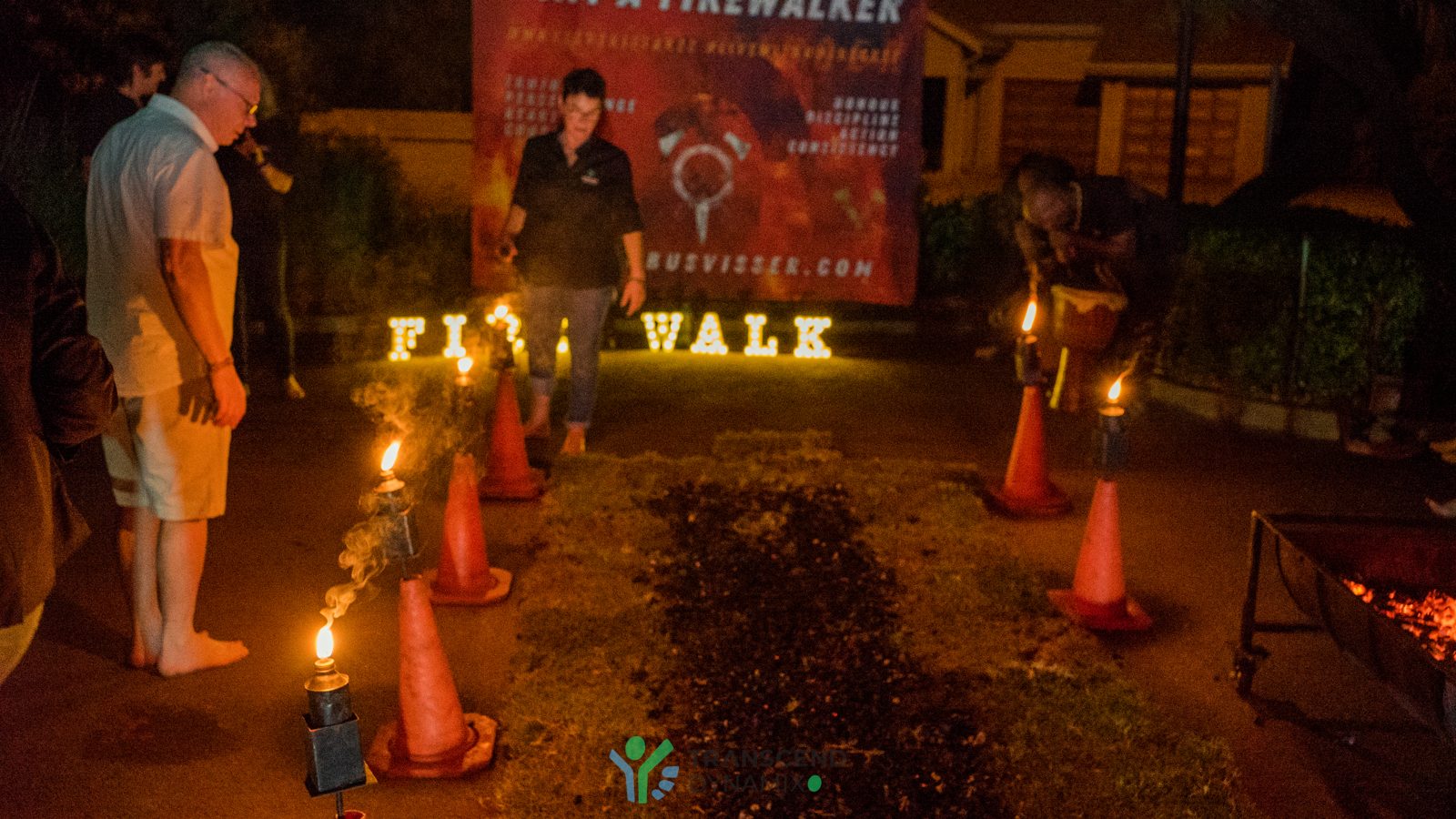 A facilitator prepares the path of coals beneath a glowing firewalk sign