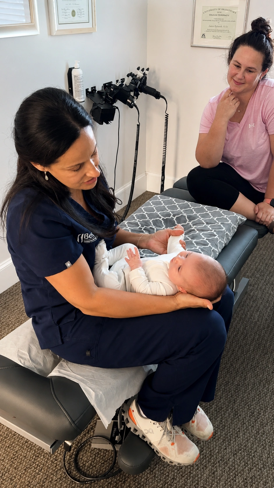 A chiropractor gently caring for a baby while the mother watches