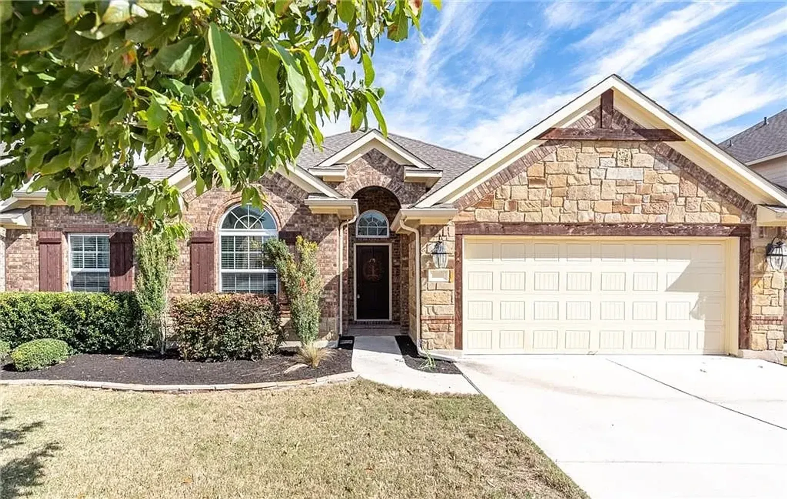 A nice single-story home with brick and a beige garage, highlighting trees in the front yard. 