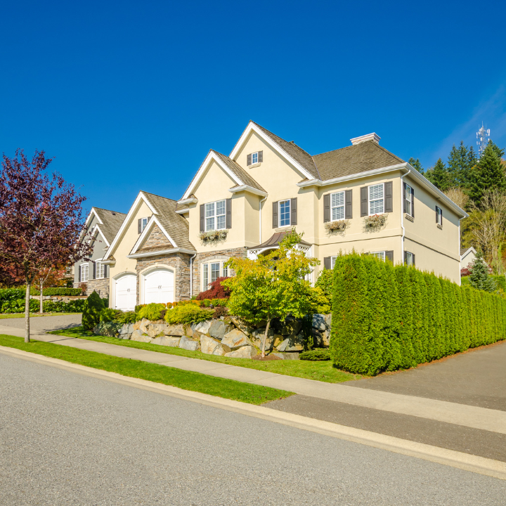 A charming yellow house with stone accents and manicured hedges, set in a picturesque neighborhood